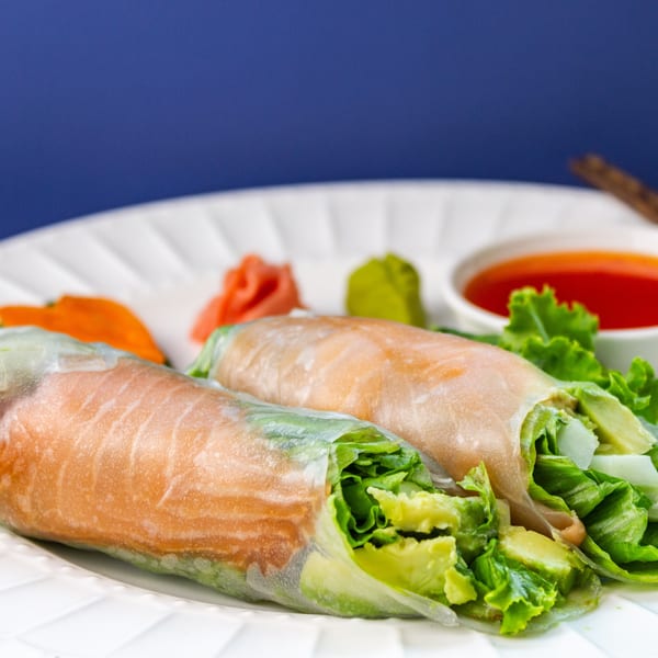 Two MAJÉ Sushi spring rolls with salmon, lettuce, and avocado, served with sauces.