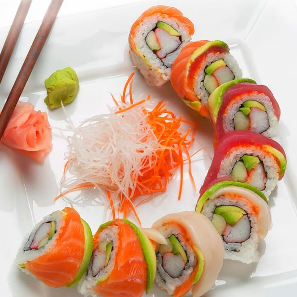 Colorful MAJÉ Sushi rolls with salmon, tuna, and avocado, served with ginger, wasabi, and shredded vegetables.