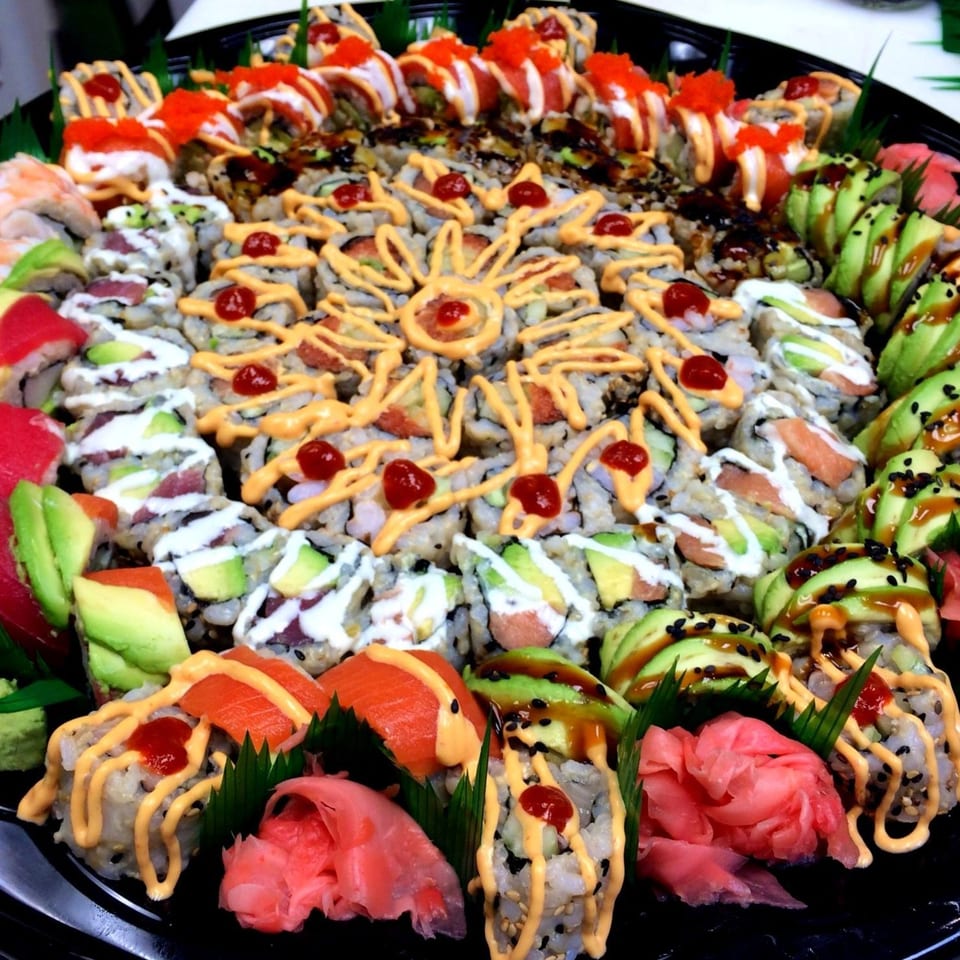 A large platter of MAJÉ Sushi rolls, artfully arranged with various toppings and sauces.