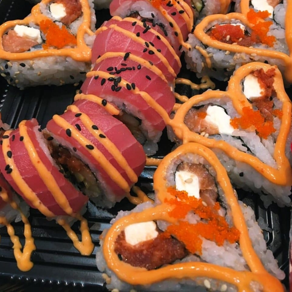 MAJÉ Sushi platter with heart-shaped sushi rolls and tuna sashimi, drizzled with orange sauce.