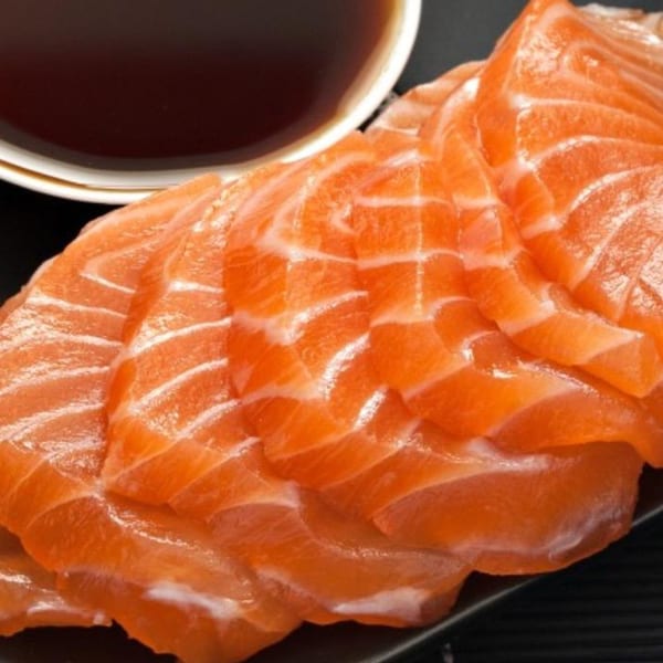 MAJÉ Sushi's fresh salmon sashimi slices, vibrant orange with white marbling, next to a bowl of soy sauce.