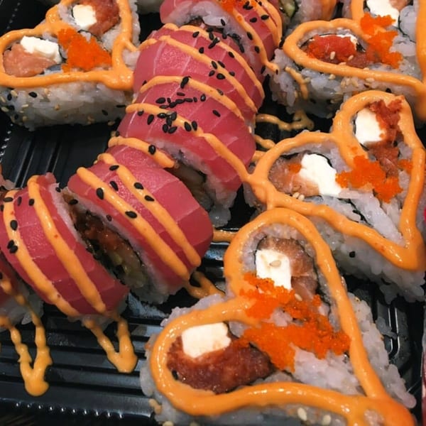 MAJÉ Sushi platter with heart-shaped sushi rolls and tuna sashimi, drizzled with orange sauce.