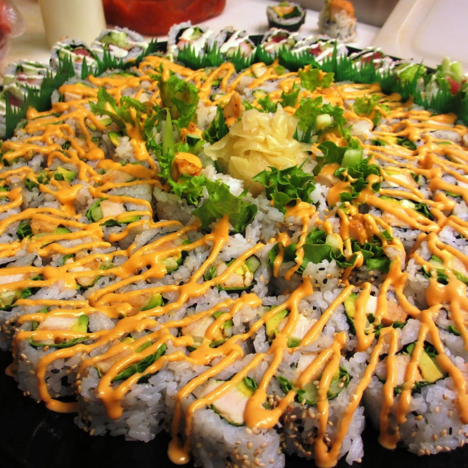 A large platter of MAJÉ Sushi rolls, drizzled with orange sauce, garnished with lettuce and ginger.