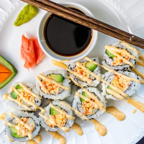 MAJÉ Sushi's California rolls with spicy mayo, soy sauce, wasabi, and pickled ginger on a white plate.