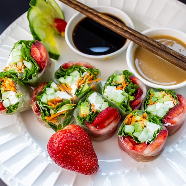 Fresh spring rolls with strawberries, cucumber, avocado, and lettuce, served with two dipping sauces.