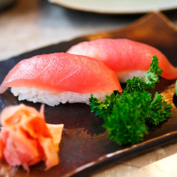 Two pieces of MAJÉ Sushi tuna nigiri with parsley and pickled ginger on a dark plate.