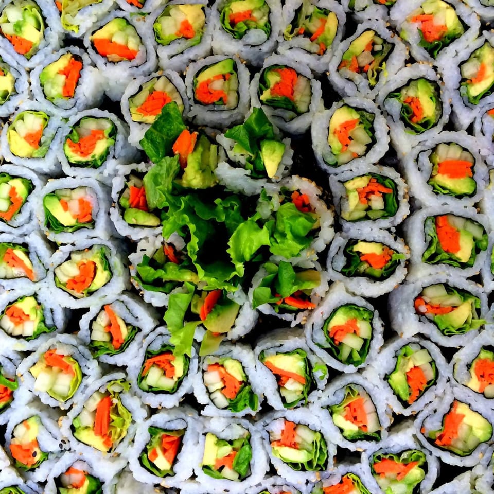 Overhead view of MAJÉ Sushi's vegetable rolls with avocado, carrots, and lettuce, arranged in a grid.