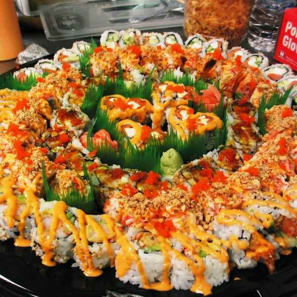 Large platter of MAJÉ Sushi rolls with various toppings, sauces, and garnishes.