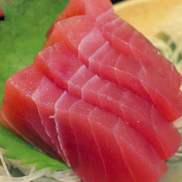 Close-up of MAJÉ Sushi's fresh, vibrant red tuna sashimi slices, artfully arranged on a green leaf.